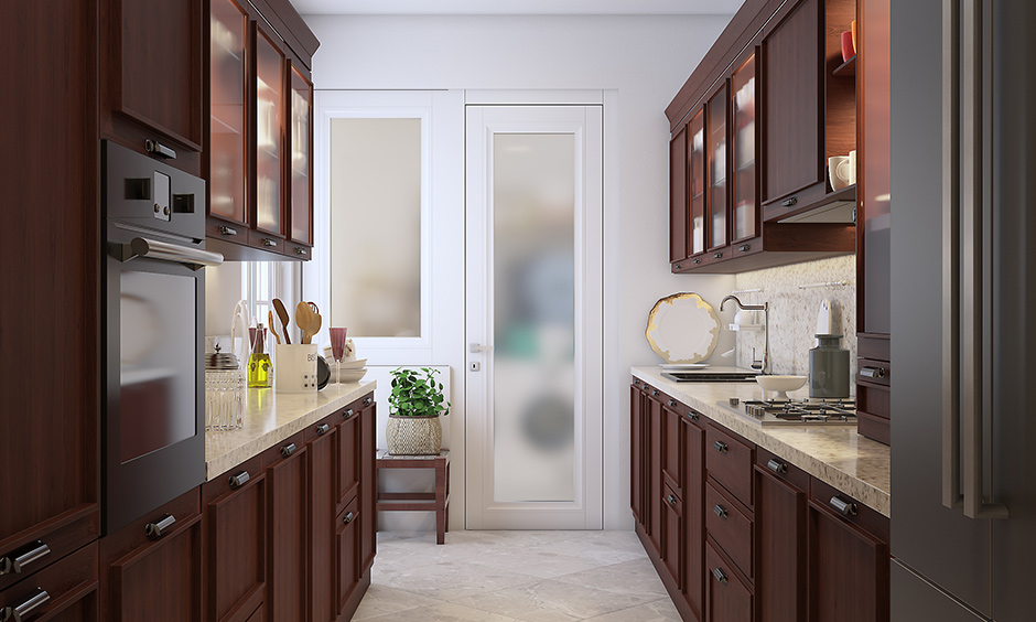 Wooden cherrywood finish modular kitchen with marble countertops and cabinets on both sides of a parallel platform design.