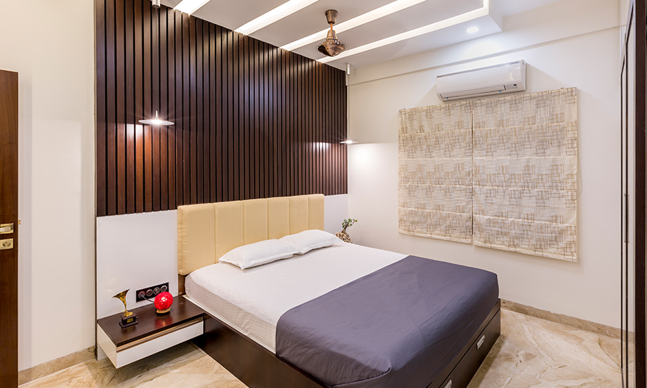 Interior design companies in Jayanagar designed this bedroom with a back panel in wooden rafters and a false ceiling.