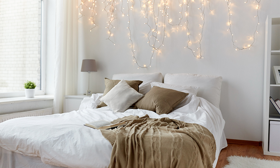 White bedroom with Queen-sized bed and dangling fairy lights for bedroom wall look lucent.